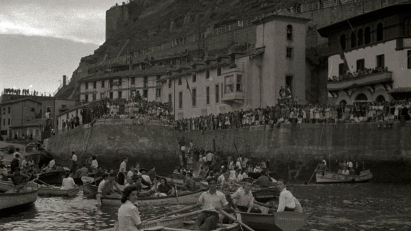 Juegos y concursos en el puerto de San Sebastián. Grupo de personas en pequeñas embarcaciones y público en el Paseo del Muelle durante la celebración de unas fiestas